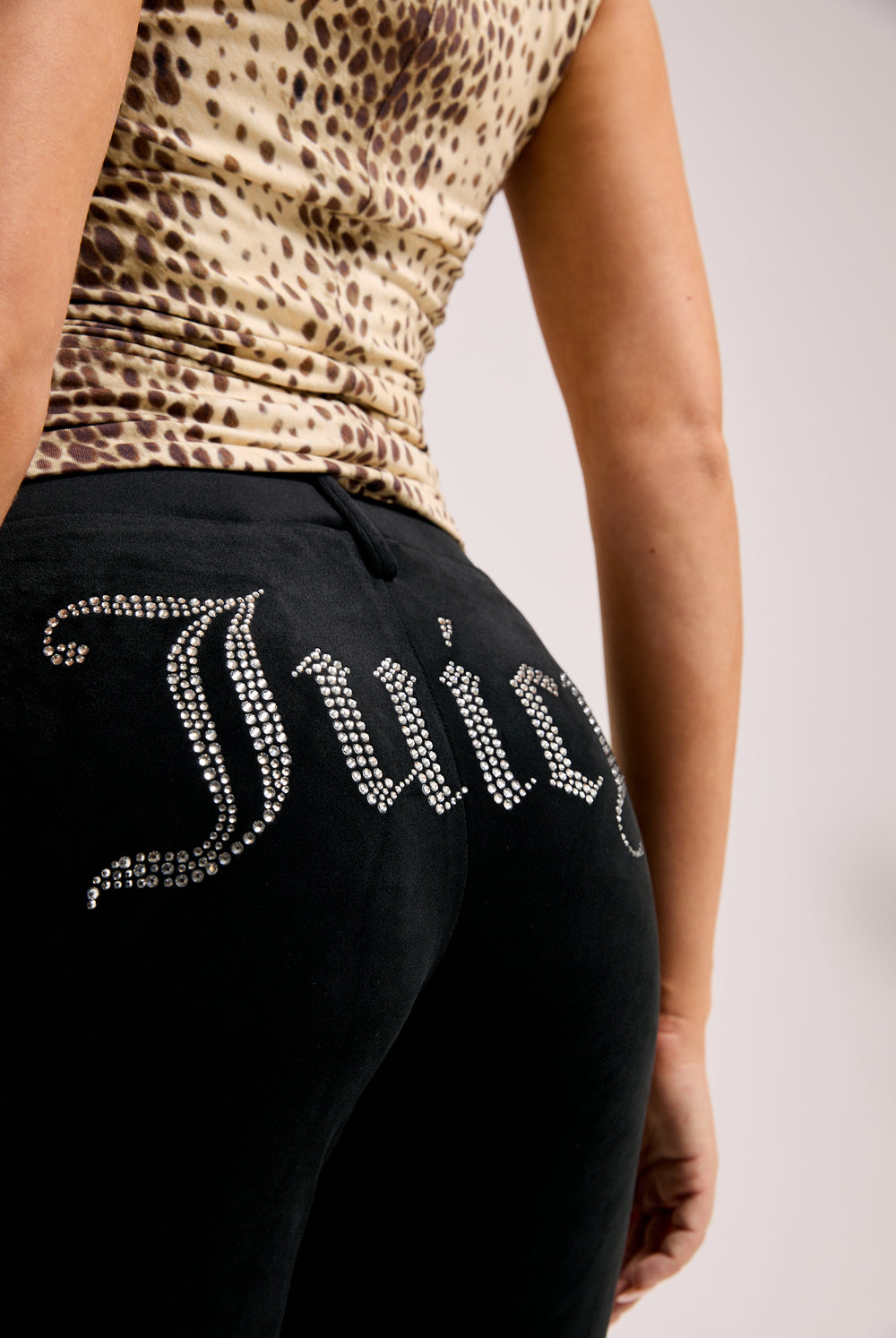 Displays a model wearing the Black Diamanté 'Juicy' branded classic velour capri pants featuring the juicy branding 