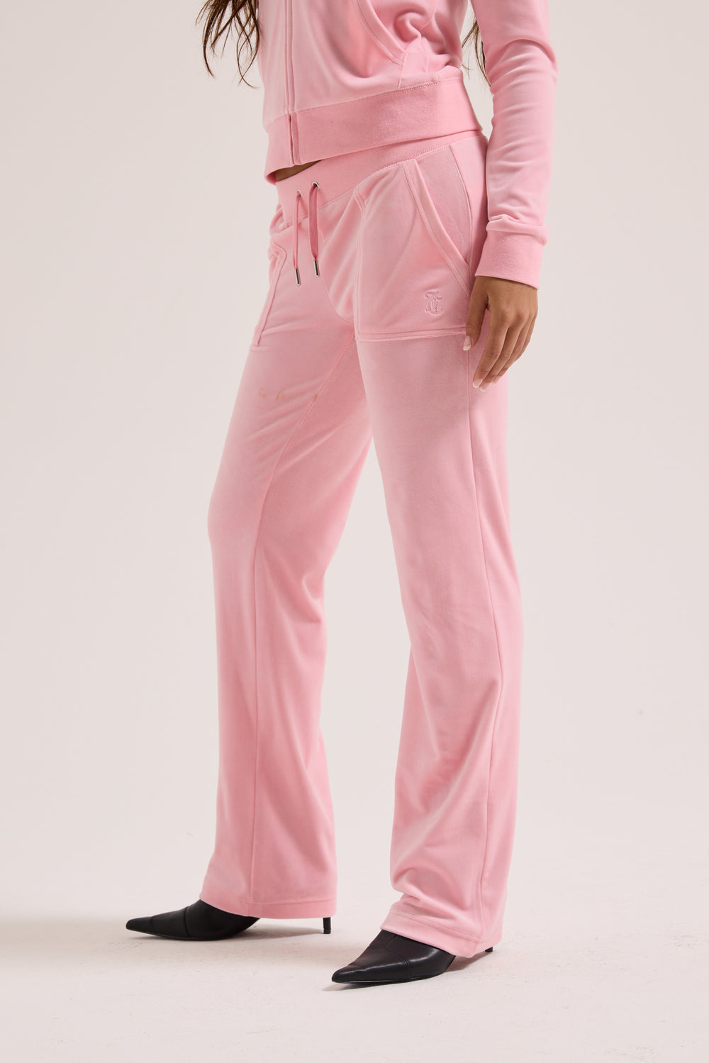 Displays a model wearing the Juicy Pink Classic 'Juicy' branded velour del ray pocketed bottoms