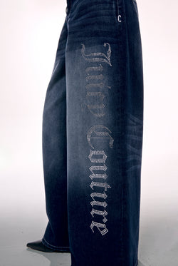 Displays a model wearing the mid Wash 'Juicy' branded wide leg Diamanté jeans featuring the juicy couture branding 