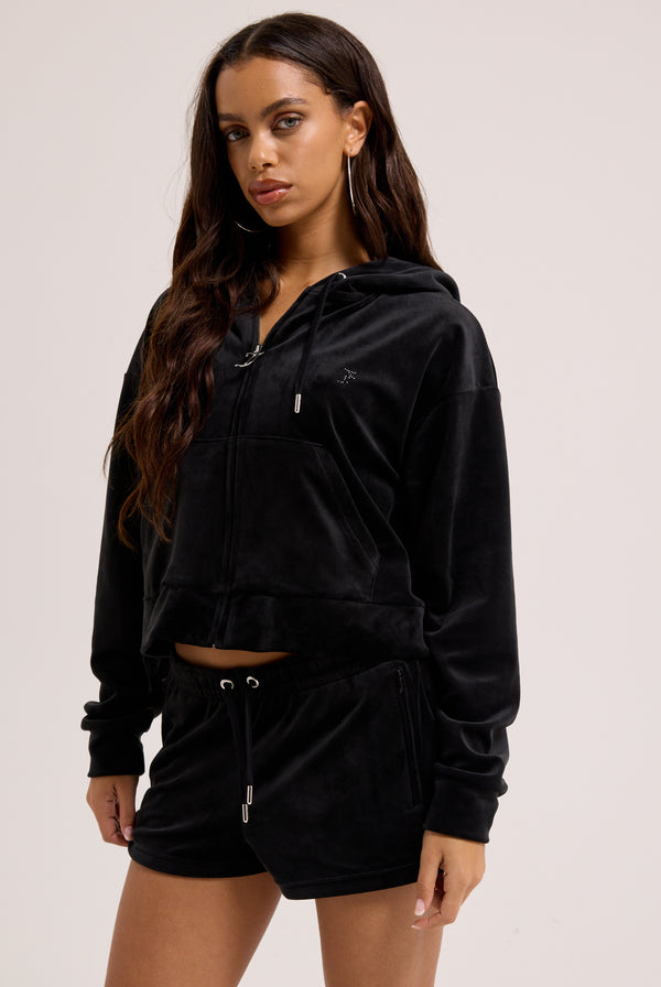 Displays a model wearing the Black outline 'Juicy' branded diamanté oversized cropped hoodie 
