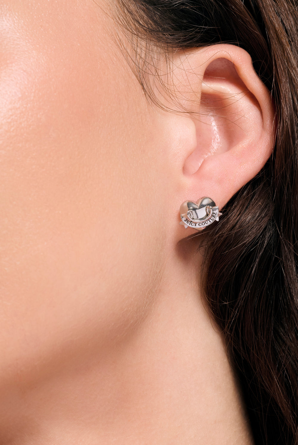Displays a model wearing the Silver Tone 'Juicy' icon heart stud earrings 