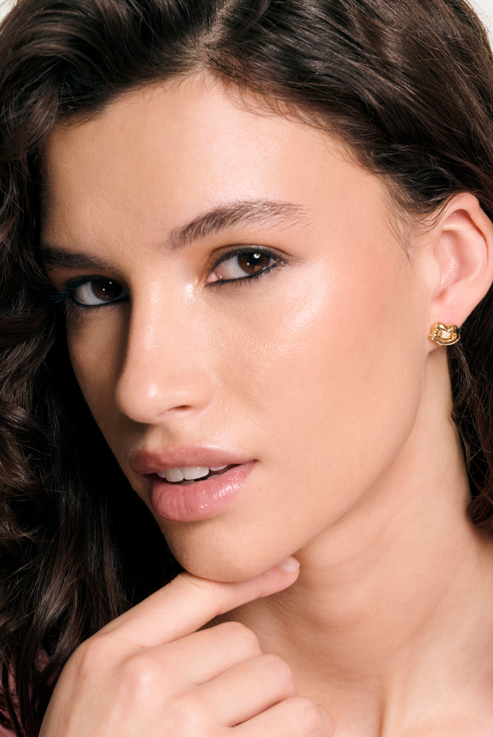 Displays a model wearing the Gold Tone 'Juicy' branded Icon heart stud earrings 