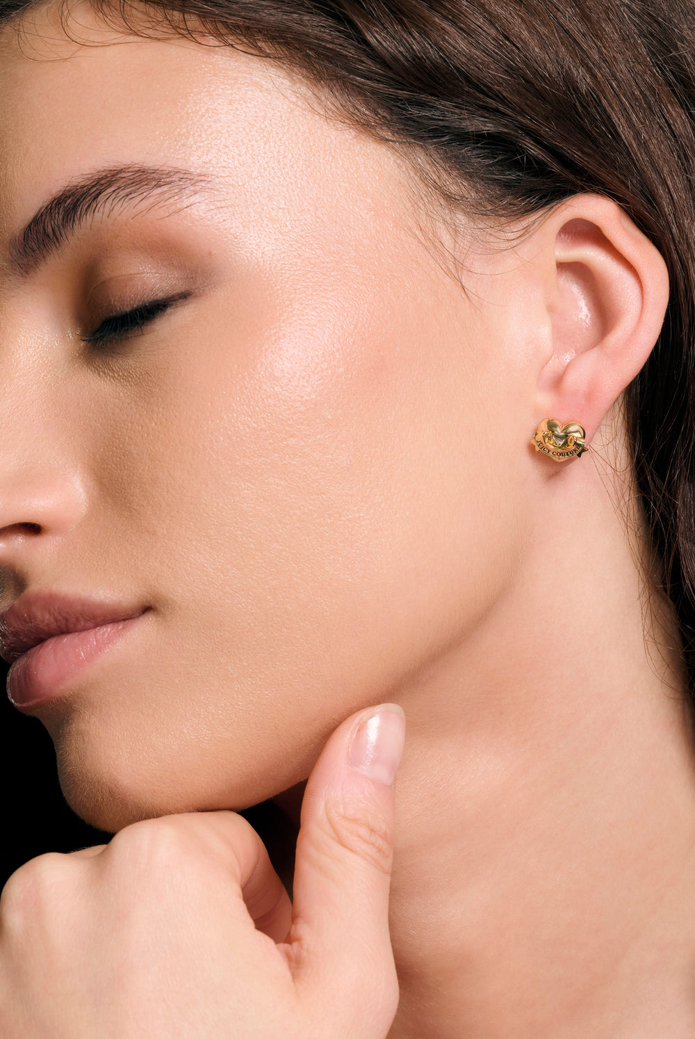 Displays a model wearing the Gold Tone 'Juicy' branded Icon heart stud earrings 