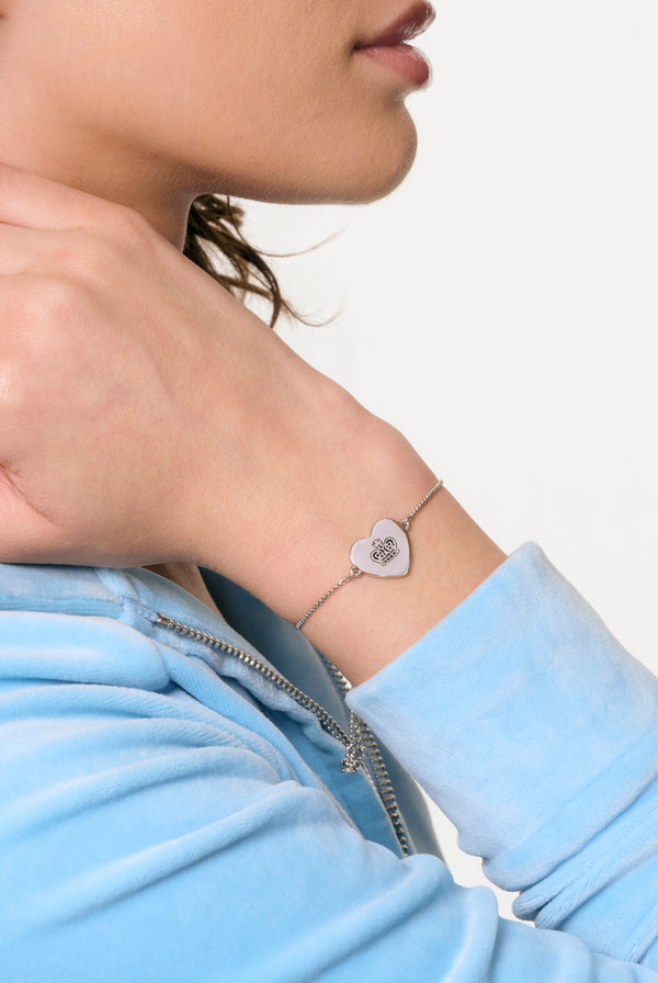 Displays a model wearing the silver tone 'Juicy' branded reversible heart adjustable bracelet 