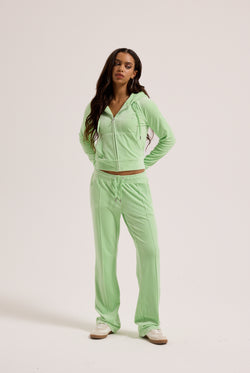 Displays a model wearing the pistachio green outline 'Juicy' branded velour diamanté tracksuit bottom 