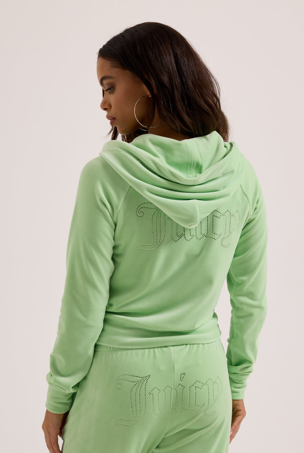 Displays a model wearing the Pistachio Green outline 'Juicy' branded diamanté velour zip-through hoodie 