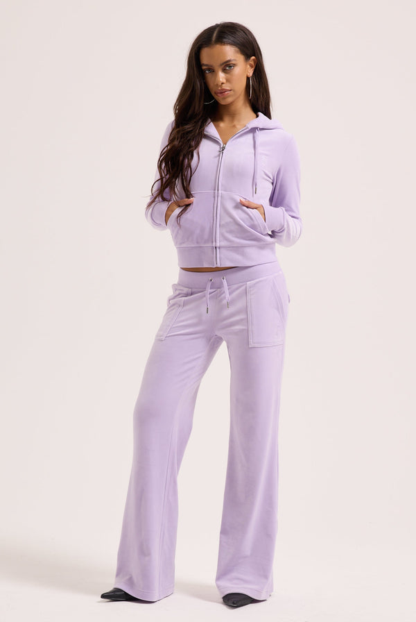 Displays a model wearing the pastel lilac 'juicy' branded low rise flare classic velour track pant 