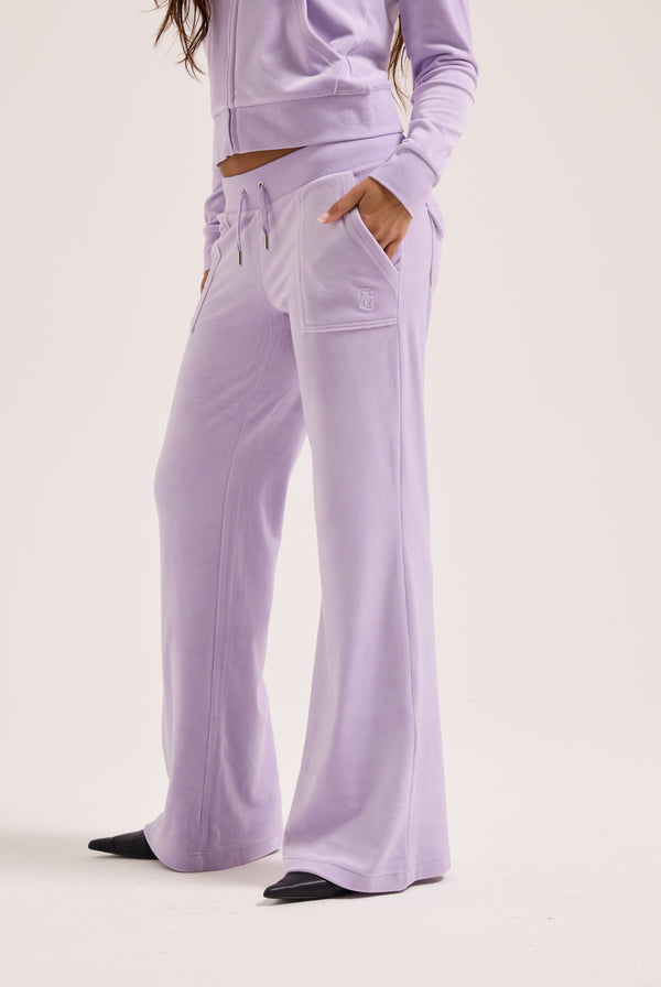 Displays a model wearing the pastel lilac 'juicy' branded low rise flare classic velour track pant 