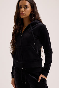 Woman wearing a black hoodie and pants on a light pink background