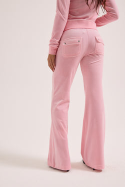 Displays a model wearing the Juicy Pink 'Juicy' branded low rise flare classic velour track pant 