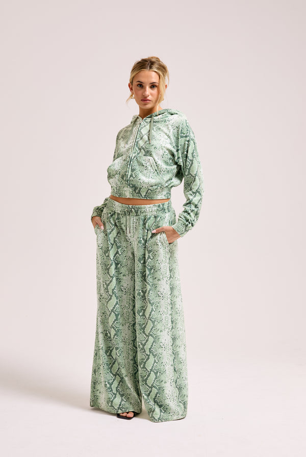 Displays a model wearing the green snake print 'Juicy' branded diamanté low rise track bottom 
