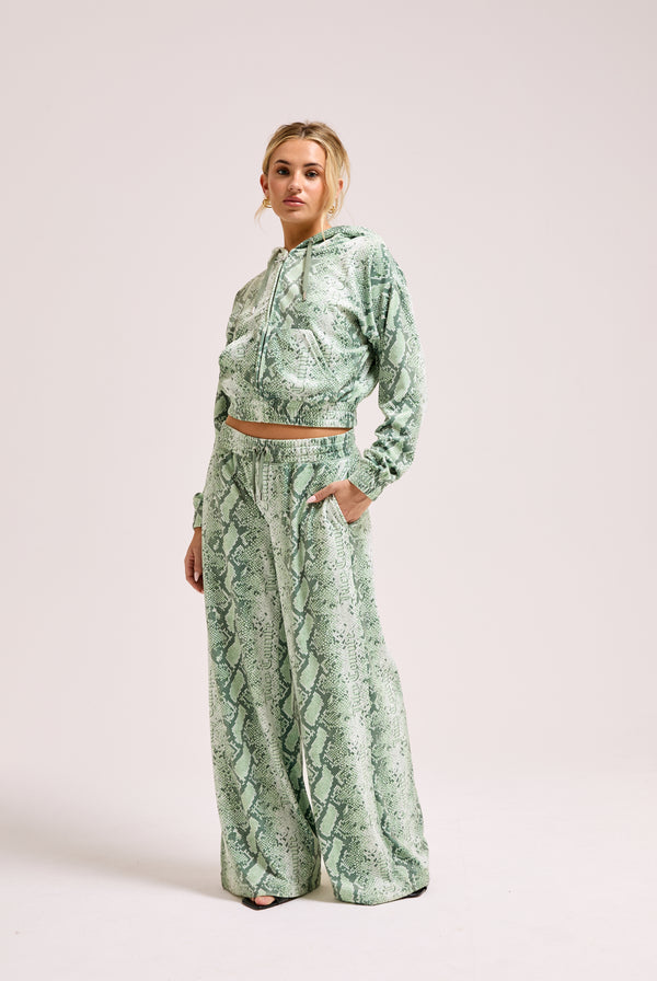 Displays a model wearing the green snake print 'Juicy' branded diamanté low rise track bottom 