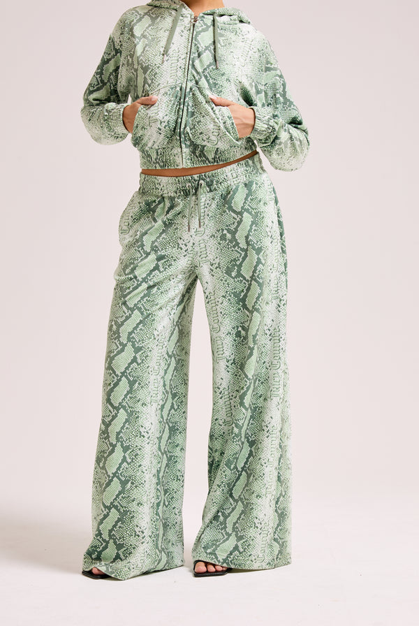 Displays a model wearing the green snake print 'Juicy' branded diamanté low rise track bottom 