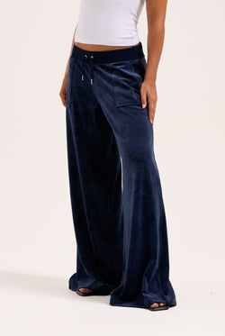 Displays a model wearing the night sky 'juicy' branded Sky Wide leg classic velour track pant 