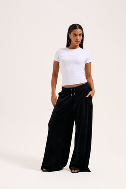 Display a model wearing the Black 'Juicy' branded wide leg classic velour track pant 